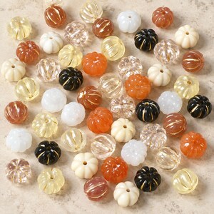 May include: A collection of small, round, pumpkin-shaped beads in various colours including clear, white, black, orange, and brown. Each bead features vertical ridges and a central hole, arranged in a scattered pattern across the frame.