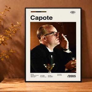 Könnte beinhalten: Ein rechteckiges Poster mit dem Filmtitel Capote in fetter schwarzer Schrift. Das zentrale Bild zeigt eine Person im schwarzen Anzug mit Brille, die eine Zigarette hält. Unter dem Bild listet der Text die Besetzung, Regie und das Jahr 2005.