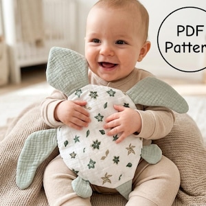May include: A soft, stuffed turtle toy made of white fabric with a green floral print and solid sage green flippers. The toy is held by a baby wearing a beige long-sleeve outfit. A circular graphic in the top right corner contains the text PDF Pattern.