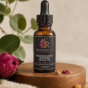 May include: An amber glass dropper bottle of FrankinRose Frankincense & Myrrh Facial Oil. The black label features a red rose graphic, gold text, and states 1 fl oz (30 mL). The bottle has a black dropper cap and contains a botanical skincare product.