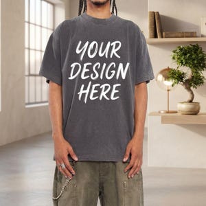 May include: A charcoal grey short-sleeved t-shirt with a crew neckline and a vintage-washed finish. The front of the shirt features the white text "YOUR DESIGN HERE" printed in a bold, hand-lettered style font across the centre of the chest.