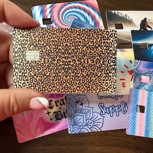 May include: A collection of colorful plastic cards with various designs, including a leopard print, a swirling pattern, a whale, and a floral design. The cards have a blank space for personalization.