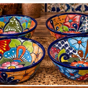 May include: A set of four round ceramic bowls featuring vibrant, hand-painted floral patterns in shades of red, blue, orange, green, and yellow. Each bowl has a solid dark blue rim and a glossy finish, displaying intricate botanical designs.