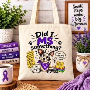 May include: A beige canvas tote bag featuring a graphic of a dog wearing a purple ribbon bandana, with the text "Did I MS something?" and "Wait... what was I doing?" alongside a checklist of items and a mug labelled "MS = Brain Fog."