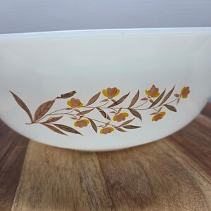 May include: A white glass mixing bowl featuring a horizontal floral pattern. The design consists of brown stems and leaves with small yellow and orange flowers arranged in a repeating botanical motif across the center of the bowl's exterior.