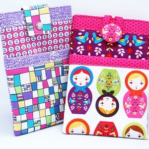 Peut inclure: Deux étuis pour tablette en tissu coloré. Un étui présente un motif géométrique en rose, bleu, vert et jaune. L'autre étui présente un fond blanc avec un motif répété de poupées russes en rose, violet, vert et rouge.