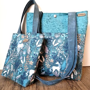 Könnte beinhalten: Zwei Tragetaschen mit einem blauen und grünen Blumenmuster mit weißen Einhörnern. Die kleinere Tasche hat ein braunes Lederetikett mit der Aufschrift "Handmade". Die größere Tasche hat ein braunes Lederetikett mit der Aufschrift "Sweet Designs".