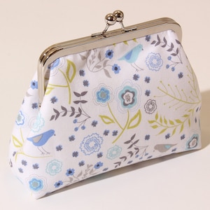May include: A white fabric clutch purse with a silver clasp. The purse has a floral pattern with blue and green birds.
