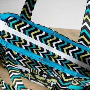 May include: A black, white, and turquoise chevron patterned tote bag with a zipper closure and two handles. The bag has a turquoise lining.