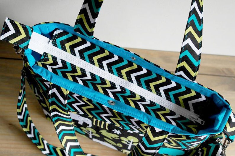 May include: A black, white, and turquoise chevron patterned tote bag with a zipper closure and two handles. The bag has a turquoise lining.
