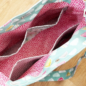May include: A turquoise and white fabric tote bag with a pink and white polka dot lining. The bag has multiple interior pockets and a long adjustable strap.