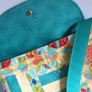 May include: A turquoise fabric crossbody bag with a floral patterned lining. The bag has a flap closure and a long adjustable strap.