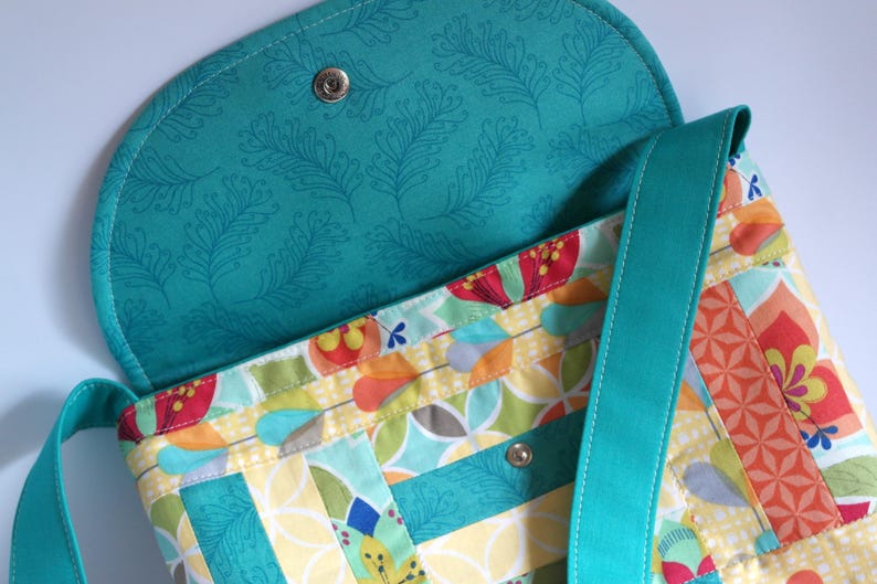 May include: A turquoise fabric crossbody bag with a floral patterned lining. The bag has a flap closure and a long adjustable strap.