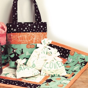 May include: A set of Halloween-themed fabric bags with a black and orange tote bag, a green and orange patchwork fabric placemat, and four small white fabric bags with black and green text. The text on the bags includes "Spooky", "Boo", "It Afr", "Loved", "Late", "Happy", "He Hou", "Um", "Black", "Are T", "Night", "Treall the free on Hel", "Things are", "Haynes".