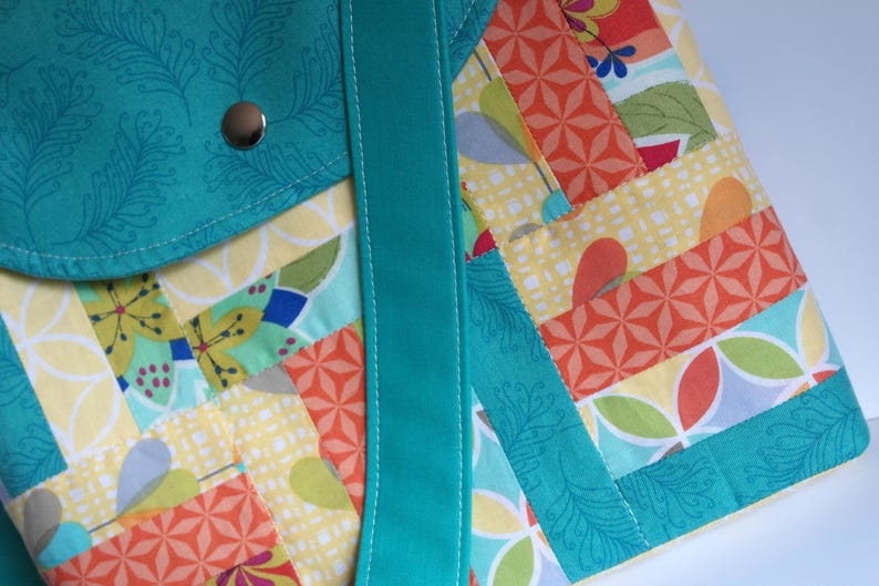 May include: A turquoise and multi-coloured patchwork tote bag with a turquoise strap. The bag has a flap pocket on the front with a silver button.