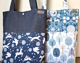 Puede incluir: Dos bolsas de mano, una con un exterior azul denim y un interior con estampado floral azul y blanco, y la otra con un exterior con estampado floral azul y blanco y un interior blanco con árboles azules y dorados. Ambas bolsas tienen una etiqueta de metal dorado con el texto "Sewn Designs".