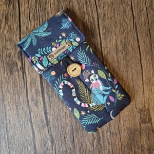 Puede incluir: Estuche para gafas de tela azul marino con un estampado caprichoso de l&eacute;mures y hojas de la jungla. El estuche tiene un cierre de bot&oacute;n de madera y una peque&ntilde;a etiqueta de cuero que dice "SusieDDesigns".