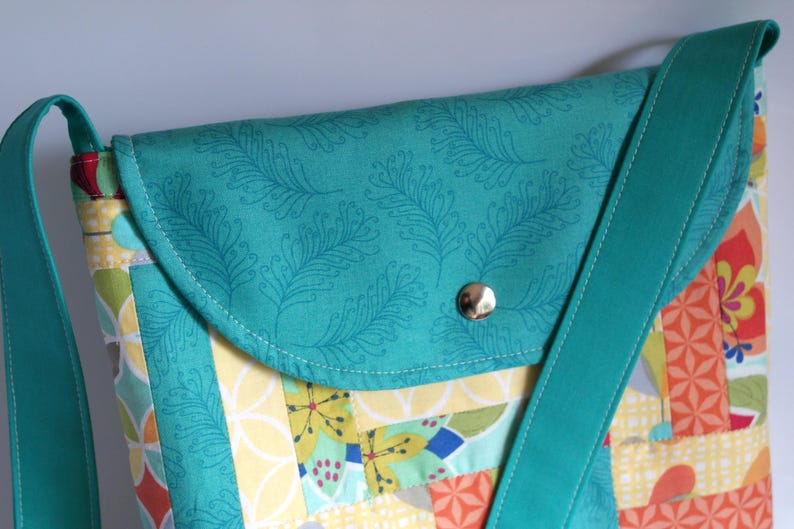 May include: A teal blue crossbody bag with a flap closure and a patterned fabric design. The bag has a teal blue strap and a silver button closure.