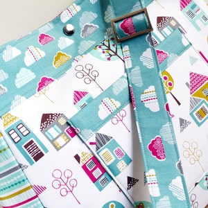 May include: A teal and white fabric tote bag with a colourful house and tree pattern. The bag has a teal strap with a silver buckle.