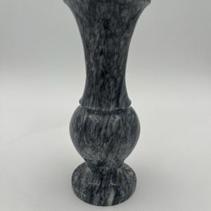 May include: A tall, slender vase crafted from dark gray and white marbled stone. The vase features a flared rim, a narrow neck, a rounded bulbous body, and a circular pedestal base, all displaying a continuous, swirling veined pattern.