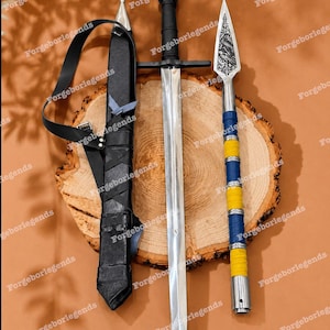 Puede incluir: Una espada de metal con empuñadura negra, una vaina de cuero negro con correa, y una lanza con hoja plateada con diseño de dragón grabado, mango envuelto en azul y amarillo y base plateada, todo sobre una rodaja de madera.