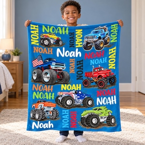 May include: A bright blue fleece blanket featuring a repeating pattern of various colorful monster trucks and the name Noah printed in multiple fonts and colors. One truck displays an American flag, while others are red, yellow, and green.