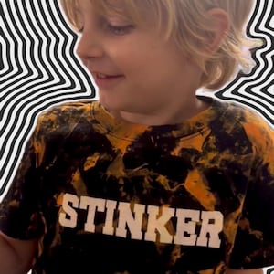 Può includere: Una t-shirt a maniche corte con un motivo tie-dye nero e arancione e la parola STINKER stampata in grassetto bianco sul petto. Il capo presenta uno scollo rotondo e una vestibilità standard, caratterizzato da un design ad alto contrasto.