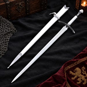 Peut inclure: Une épée argentée avec une poignée blanche et un fourreau blanc assorti. L'épée présente une lame pointue, une garde avec des détails décoratifs sombres et un pommeau. Le fourreau comprend une attache de sangle blanche près de l'ouverture.