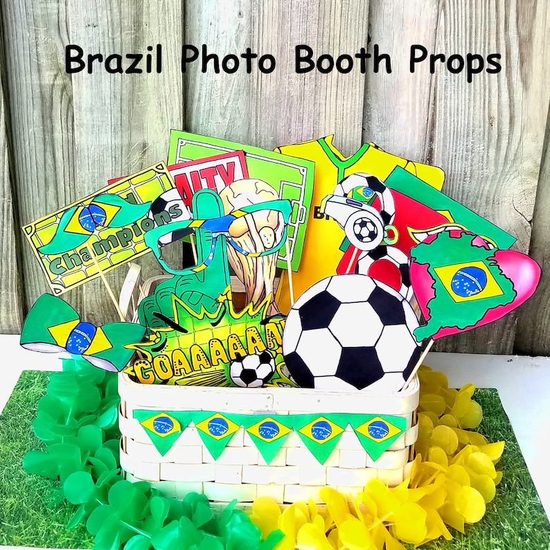 May include: A set of Brazil-themed photo booth props, including a soccer ball, a green and yellow bow tie, a pair of glasses, a sign that says "Champions", and a sign that says "GOAAAAAAAAL". The props are in a white wicker basket with green and yellow Brazilian flag bunting.