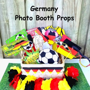 May include: A basket filled with photo booth props for a Germany-themed party. The props include a soccer ball, a mustache, a heart with the German flag, and a sign that says "World Champions".