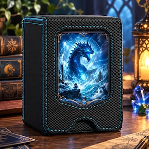May include: A black deck box with a textured finish and bright blue stitching. The front features a rectangular inset displaying a vibrant illustration of a blue dragon rising from stormy ocean waves, with a small figure standing on a rocky shore.