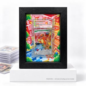 May include: A black wooden frame containing a graded Charmander trading card. The card is encased in a clear plastic slab with a label reading 2021 Black Star Promo Charmander 10 Gem Mint. The background features a colourful pixelated art print.