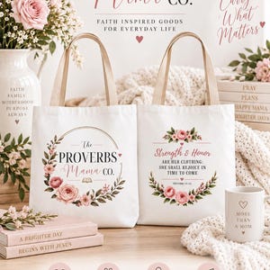 May include: Two white canvas tote bags with beige handles. The left bag features a floral wreath surrounding the text The PROVERBS Mama CO. The right bag displays the text Strength & Honor ARE HER CLOTHING: SHE SHALL REJOICE IN TIME TO COME.
