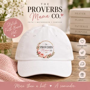 Puede incluir: Una gorra de béisbol blanca con un gráfico de corona floral circular que rodea el texto The Proverbs Mama Co. El diseño incluye rosas de color rosa y melocotón con hojas verdes. La gorra tiene una corona estructurada y una visera curva.