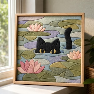 May include: A square fabric wall art piece in a light wood frame featuring a quilted scene of a black cat with yellow eyes peeking out of a pond. The water is composed of blue and purple fabric patches with pink lotus flowers and green lily pads.