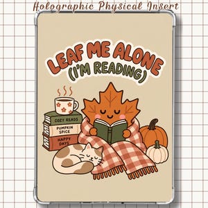 Pode incluir: Uma capa retangular para tablet com fundo bege e uma ilustração gráfica de uma folha de bordo sorridente lendo um livro enrolada num cobertor xadrez. O texto LEAF ME ALONE (I'M READING) está acima de livros, um gato e abóboras.