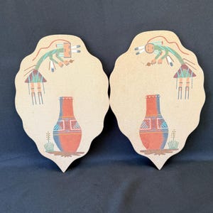May include: Two scalloped, tan-colored wall plaques featuring identical illustrations of a stylized figure in green and red attire positioned above a large, orange-red ceramic vase with blue and white geometric patterns and green plant accents.