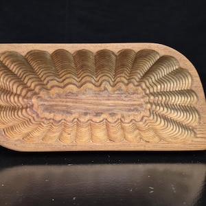 May include: A rectangular wooden mold with rounded corners and a flat base, featuring a deeply carved interior with a repeating scalloped or fluted pattern along the edges and a smooth, flat, rectangular center section made of natural brown wood.