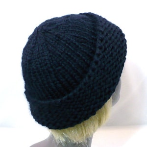 May include: A solid black knit beanie cap featuring a thick, chunky yarn texture with a prominent folded cuff at the base. The hat is constructed with a vertical ribbed stitch pattern that extends from the crown down to the wide, rolled brim.
