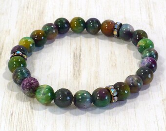 May include: A stretch bracelet composed of round, polished beads in shades of green, purple, and brown. The bracelet features two metallic spacer beads encrusted with small, clear, iridescent crystals positioned at intervals along the circular strand.