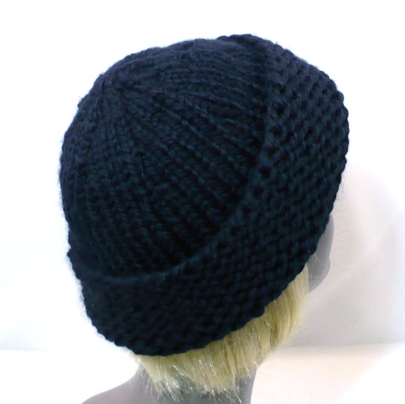 May include: A solid black knit beanie cap featuring a thick, chunky yarn texture with a prominent folded cuff at the base. The hat is constructed with a vertical ribbed stitch pattern that extends from the crown down to the wide, rolled brim.