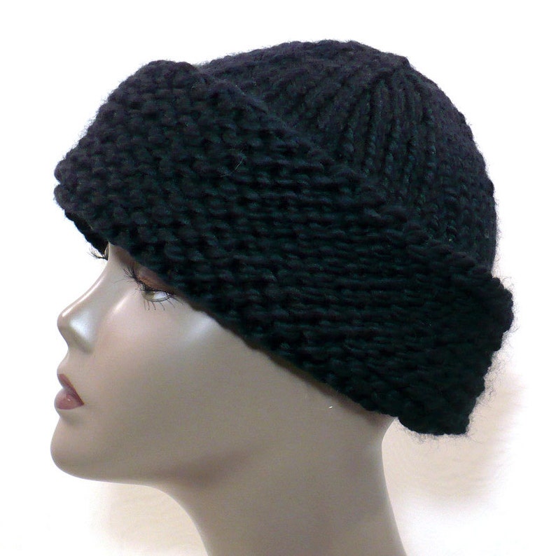 May include: A solid black knit beanie with a thick, folded brim. The hat features a chunky, textured yarn construction with a ribbed pattern on the crown and a garter stitch texture on the wide cuff, providing a dense and warm appearance.