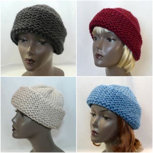 May include: A collection of four chunky knit beanies in dark gray, deep red, beige, and light blue. Each hat features a thick, folded brim and a textured, garter stitch pattern, providing a warm and substantial appearance for cold weather.