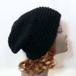 May include: A solid black knit beanie hat with a textured, chunky stitch pattern. The hat features a slouchy, rounded silhouette that covers the crown of the head, crafted from a thick yarn material with a consistent dark color throughout the design.