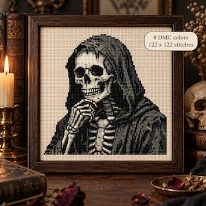 May include: A framed cross-stitch embroidery featuring a skeletal figure in a hooded robe, with one hand resting near the chin. The design uses 8 DMC colors and measures 122 x 122 stitches. The artwork is displayed in a dark brown wooden frame.