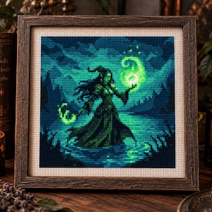 May include: A square cross-stitch embroidery in a dark wooden frame depicting a figure in a long flowing robe standing in water. The figure holds a glowing green orb of light in one hand and a curved staff in the other, set against a dark blue background.