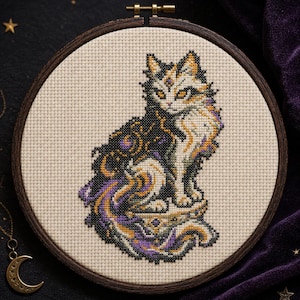 Puede incluir: Un bordado de punto de cruz en un bastidor de madera circular que muestra un gato con pelaje blanco, negro y morado. El diseño del gato incorpora patrones celestiales, incluyendo estrellas y formas cósmicas en tonos dorados y morados.