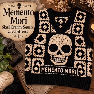 Könnte beinhalten: Eine schwarz-cremefarbene Häkelweste mit einem großen Totenkopfmotiv auf der Vorderseite, umgeben von kleineren floralen Granny Squares. Das Kleidungsstück hat einen V-Ausschnitt, gerippte Säume und den Schriftzug MEMENTO MORI in cremefarbenen Buchstaben.