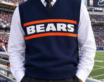 May include: A navy blue V-neck sweater vest featuring the word BEARS in white block letters, flanked by two horizontal orange stripes across the chest. The vest is worn over a crisp white long-sleeved button-down shirt with a black necktie.
