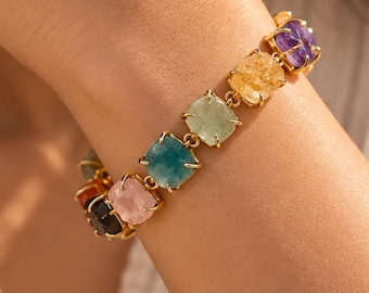 Puede incluir: Una pulsera de tono dorado que presenta una serie de piedras preciosas de corte cuadrado y multicolor, incluyendo tonos morados, amarillos, verde claro, azules, rosas y gris oscuro, cada una en un engaste de garras unido por eslabones dorados.
